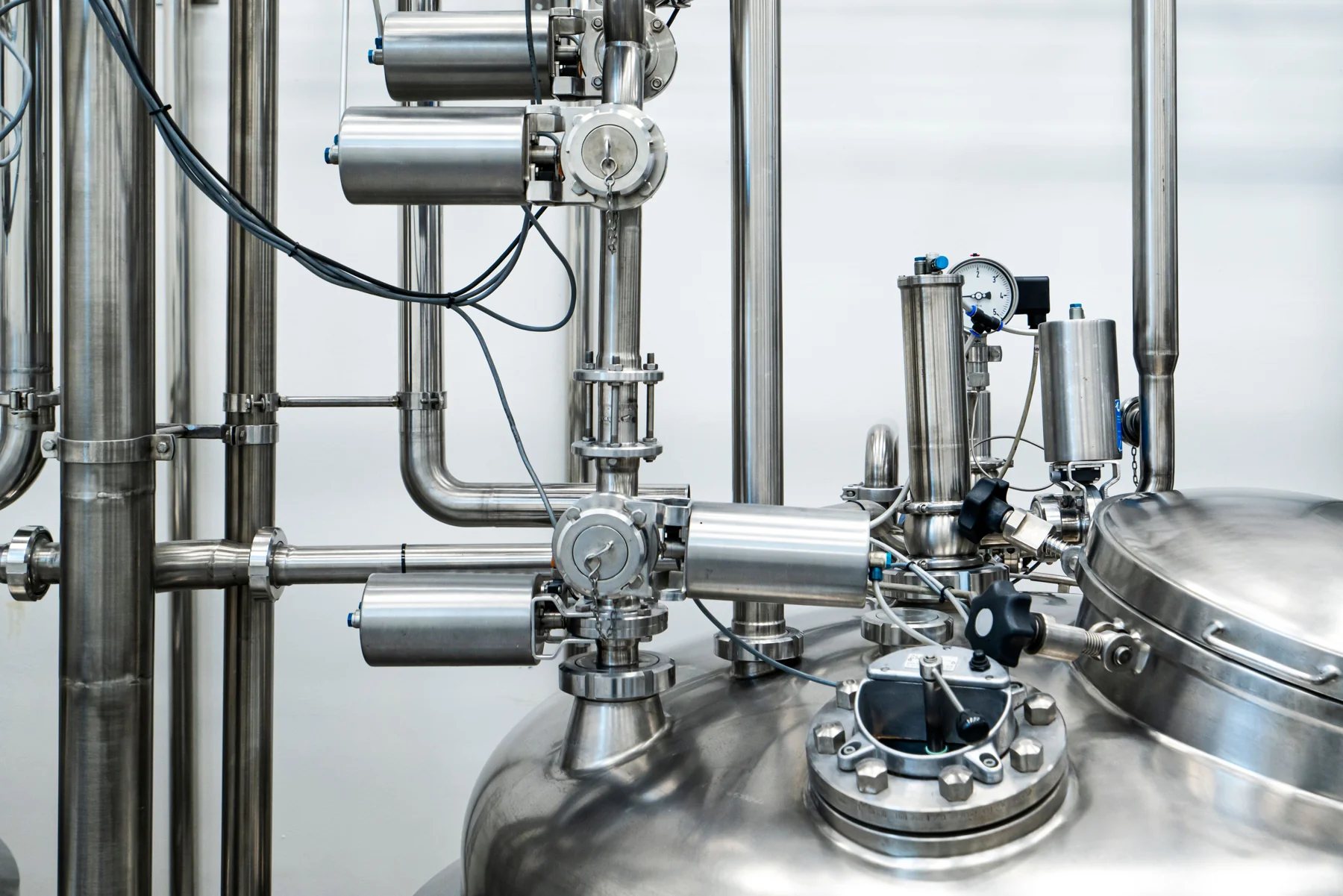 Stainless steel process vessels with pressure gauge, valves and connecting pipework in an industrial interior